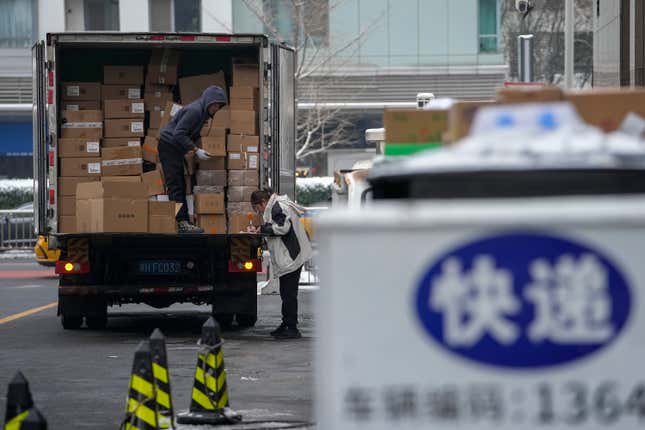 A worker unloading food products as a woman checking the stock lists at a loading area outside a shopping mall in Beijing, Tuesday, Dec. 12, 2023. Chinese leaders have wrapped up a two-day annual meeting to set economic priorities for the coming year, the official Xinhua News Agency reported Tuesday without giving details of what was decided. (AP Photo/Andy Wong)