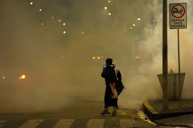 A demonstrator surrounded by a cloud of teargas, takes photos with his mobile phone during a protest against a recently approved mining contract between the government and Canadian mining company First Quantum, in Panama City, Tuesday, Oct. 31, 2023. (AP Photo/Arnulfo Franco)