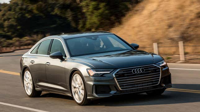 A gray Audi A6 driving on a road near a hill