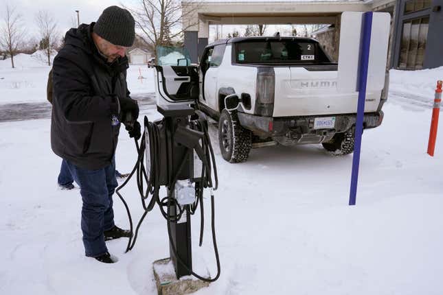 A man plugging a white Hummer EV into a public charging station in the snow