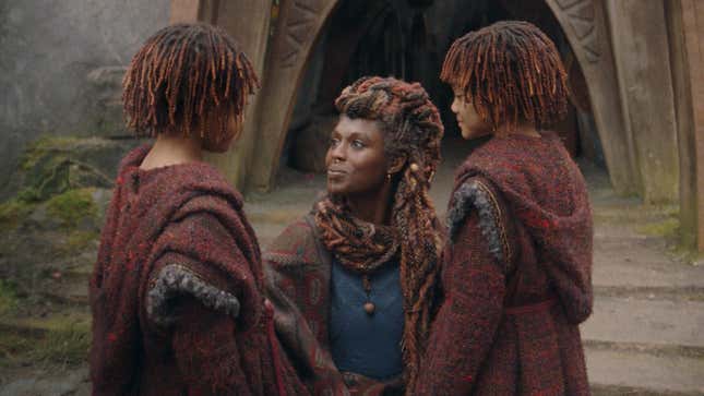 A woman kneels before two children with similar hairstyles and garb in an image from The Acolyte.