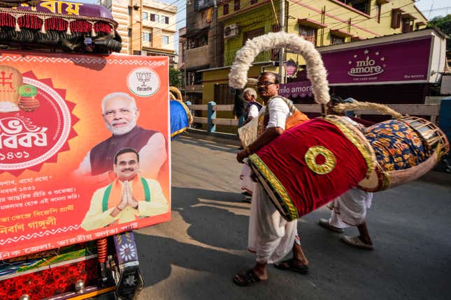 Drummers walk alongside a vehicle with hoardings showing portraits of Indian Prime Minister Narendra Modi and the local Bharatiya Janata Party (BJP) candidate Anirban Ganguly, during an election rally for the forthcoming national parliamentary election in Kolkata, India, Sunday, April 14, 2024. (AP Photo/Bikas Das)