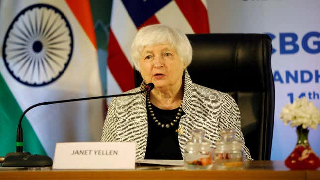 US Treasury Secretary Janet Yellen speaks into a microphone from behind a desk. A placard in front of her has her name on it.