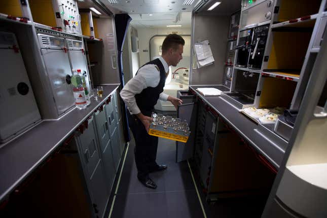 A Deutsche Lufthansa AG cabin crew member carries a tray of drinking glasses in the kitchen of a Boeing 747-8 passenger aircraft, manufactured by Boeing Co., as the German airline unveil its new premium economy class service during a flight over Frankfurt, Germany, on Thursday, Oct. 2, 2014