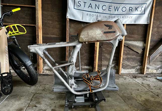 The bare frame and gas tank of a 1969 Honda CB350 in a sad dingy garage.