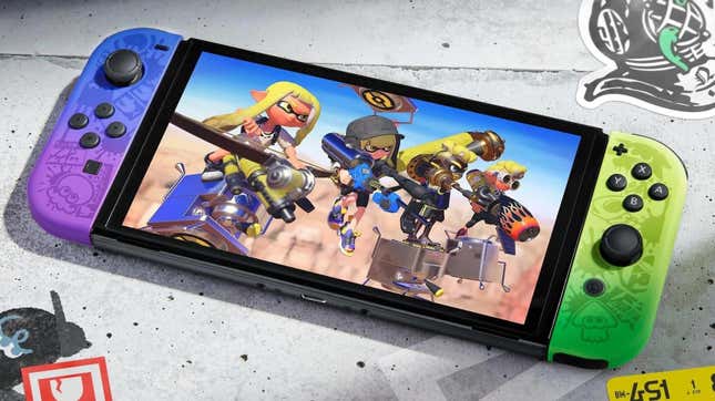 A Splatoon 3-themed Switch OLED model sits on concrete as its characters line-up onscreen. 