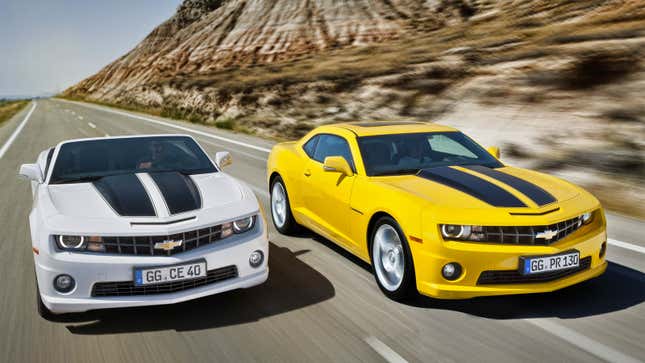 A photo of a white and a yellow Chevrolet Camaro driving on a highway. 