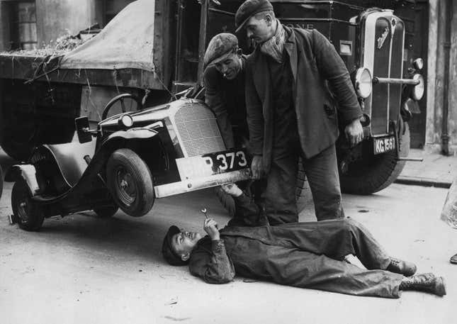 Instead of using a car jack to carry out repairs on a one horsepower midget car, a mechanic in Cardiff simply gets a couple of helping hands to lift up the front of the vehicle