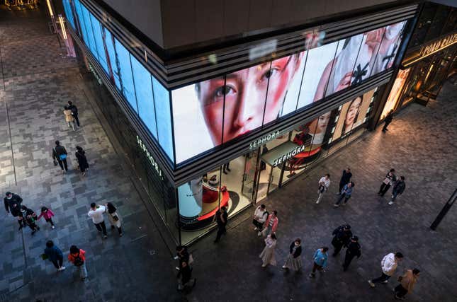 A view from above of a sleek-looking shopping mall where pedestrians walk past a Sephora at night.