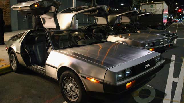 A photo of three Delorean cars parked with the gulwing doors open. 