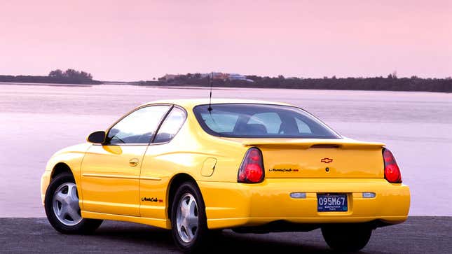 A photo of a yellow Chevrolet Monte Carlo parked next to a lake. 