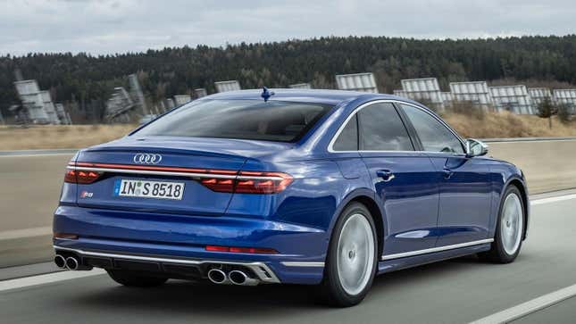 A blue Audi S8 from the rear 3/4 angle driving in front of a tree covered hill