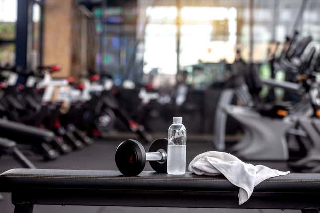Dumbbell, water bottle, towel on the bench in the gym. - stock photo