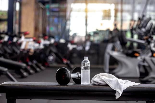 Haltère, bouteille d’eau, serviette sur le banc dans la salle de gym. - photo photo