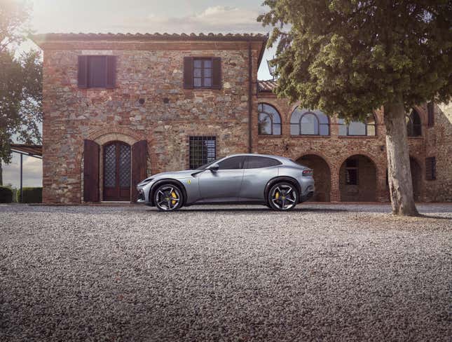 A gray 2024 Ferrari Purosangue SUV is parked on gravel in front of a large European villa.