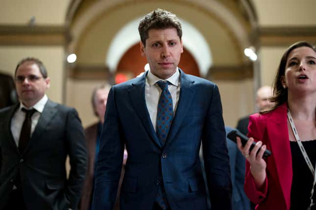 Sam Altman au centre portant un costume bleu marine et marchant à côté d’une femme brune avec un blazer rose