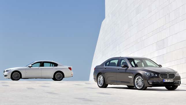 A photo of two BMW 7 Series sedans parked against a white wall. 