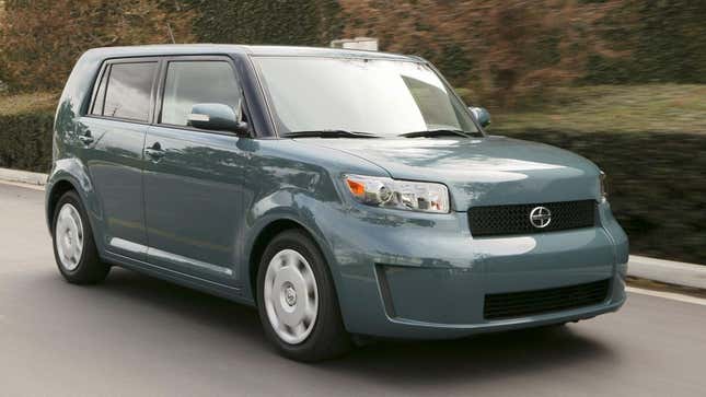 Une Scion xB de deuxième génération bleu sarcelle roulant devant des haies