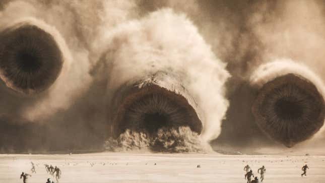 Multiple sandworms streak towards people running on the sand.