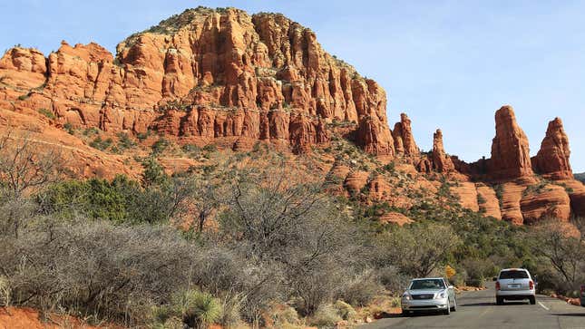 A photo of two cars driving past a mountain on a road in Arizona. 