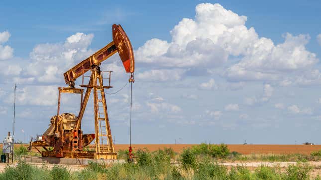 An oil pump jack digs in front of a clouded blue sky