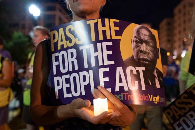 In this July 17, 2021, file photo, a person holds a candle and a poster with an image of the late Rep. John Lewis during a rally in support of voting rights, at Black Lives Matter Plaza in Washington.