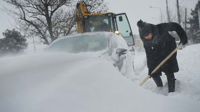 A photo of someone digging a car out of a snowdrift. 