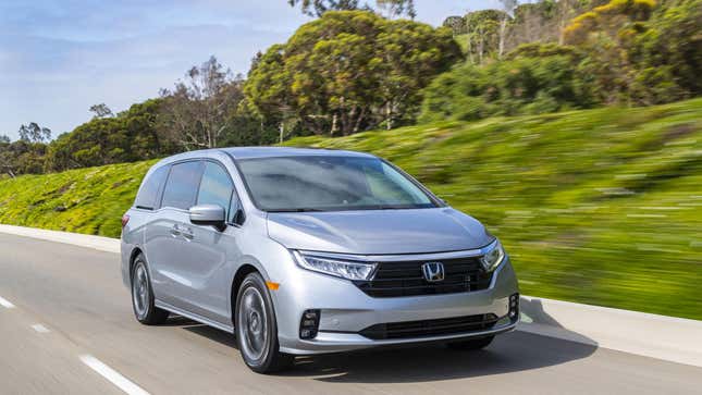 A silver Honda Odyssey driving in front of a grassy knoll