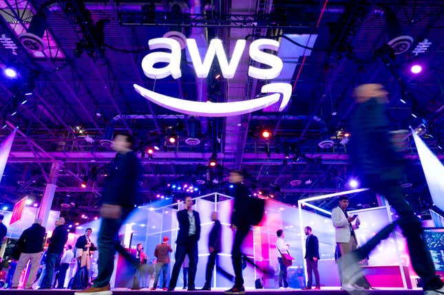 white aws logo hangs above people walking around an expo that is lit up purple