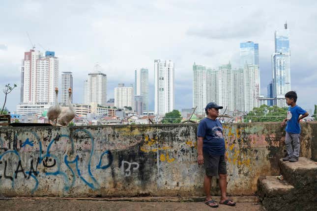 A man talks to a boy as the city skyline is seen in the background at a lower-income neighborhood in Jakarta, Indonesia, Wednesday, Feb. 7, 2024. A presidential election in Indonesia, the world&#39;s third-largest democracy, is highlighting the choices to be made as the country seeks to exploit its rich reserves of nickel and other resources that are vital to the global transition away from fossil fuels. (AP Photo/Achmad Ibrahim)