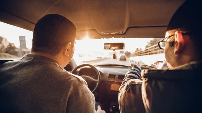 Caucasian man driving A Car while his friend comment his driving.