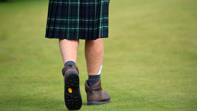 A man walks across a field wearing a kilt. 