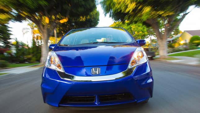 A head-on shot of a blue Fit EV driving on a residnetial street