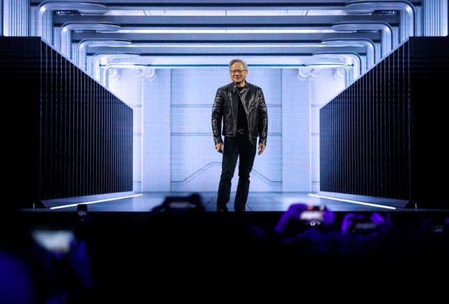 Jensen Huang standing on stage wearing an all black outfit including his signature black leather motorcycle jacket, there's a graphic behind him that looks like a hallway in a data center, phones can be seen at the bottom of the photo of people taking photos of Jensen