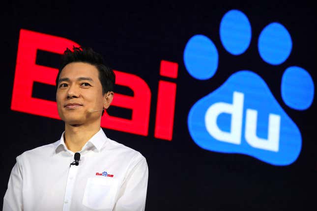 gros plan de Robin Li portant un microphone et une chemise blanche avec le logo Baidu, le logo Baidu est affiché derrière lui, le du dans le mot est dans une empreinte de patte de chien bleue