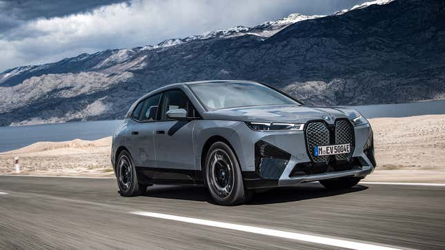 Front view of the BMW iX in motion on a road near a lake.