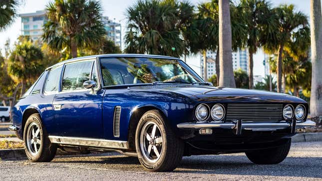 Una foto de un Jensen Interceptor azul estacionado frente a unas palmeras