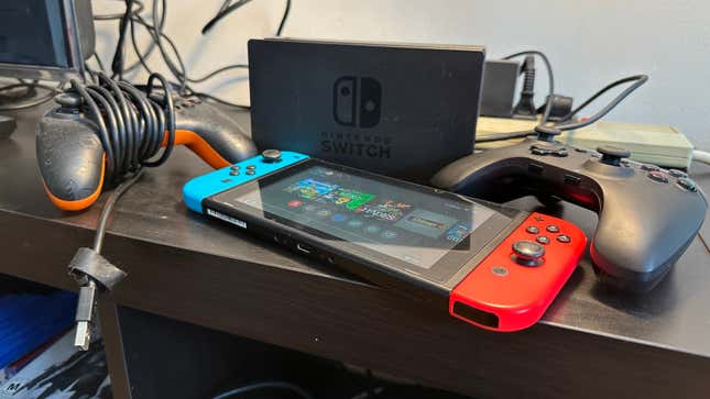 A Nintendo Switch console on a TV cabinet surrounded by controllers and the Switch dock.