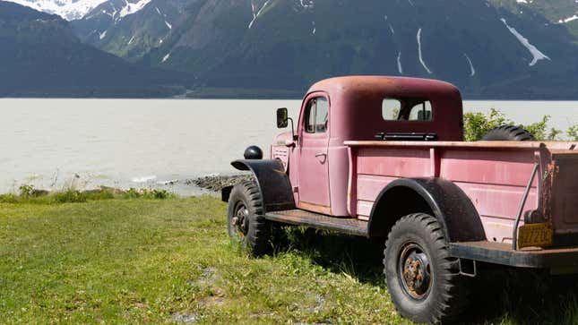 A photo of an old pickup truck parked by a lake. 