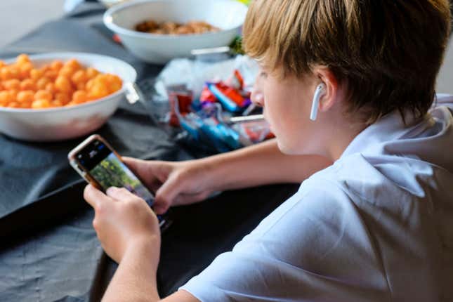 A pre-teen boy concentrating on smartphone with ear buds and bowls of snacks.