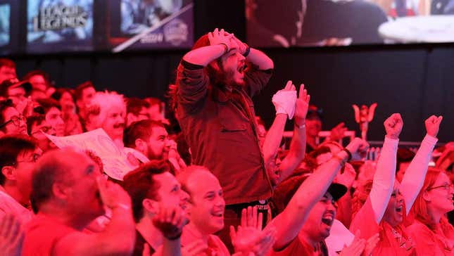 A League of Legends fan stands up in a crowd and holds their head in disbelief. 