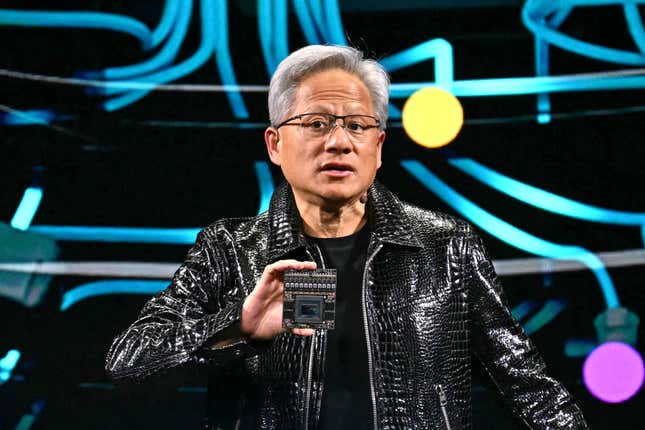 Jensen Huang, con una chaqueta de cuero negra, habla y sostiene un chip frente a una pantalla con líneas de neón azul y luces de colores.