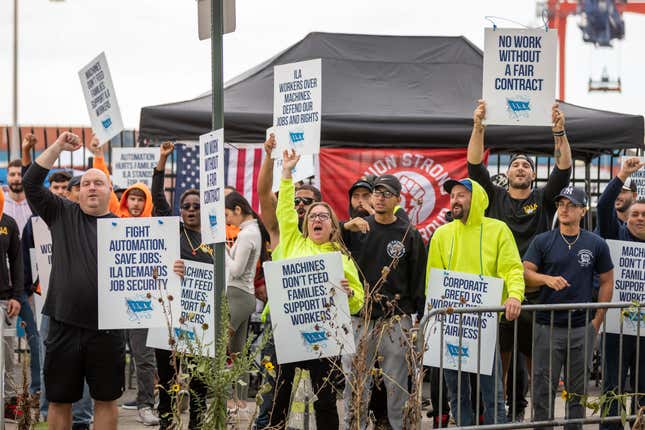 Workers hold signs reading "Fight Automation. Save Jobs. ILA Demands Job Security," "No Work Without a Fair Contract," "Machines Don't Feed Families. Support ILA Workers," and "Corporate Greed Over Workers' Rights. ILA Demands Fairness."