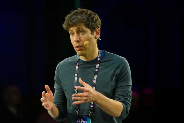 Sam Altman wearing a forest green long-sleeved shirt and a lanyard, speaking with his hands up into a face mic