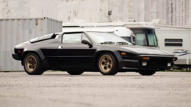 Un Lamborghini Jalpa negro estacionado frente a vehículos recreativos