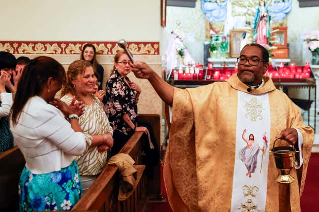 Father Ako Walker sprinkles holy water on parishioners during Easter Mass at Sacred Heart of Jesus and Saint Patrick, Sunday, March 31, 2024, in Baltimore, Md. (AP Photo/Julia Nikhinson)