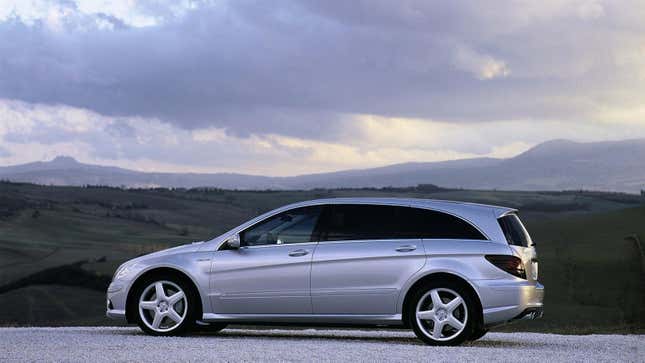 A silver R63 AMG from the side angle parked in front of rolling green hills