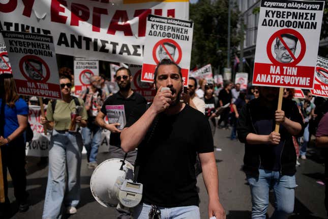 A protester using a loudspeaker shouts slogans during a rally in Athens, Greece, Wednesday, April 17, 2024. A 24-hour strike called by Greece&#39;s largest labor union have halted ferries and public transport services in the Greek capital and other cities, to press for a return of collective bargaining rights axed more than a decade ago during a severe financial crisis. Writing on banner with red line across the face of Greece’s Prime Minister, Kyriakos Mitsotakis, reads in Greek; “Killer Government / We Will Overturn It”. (AP Photo/Thanassis Stavrakis)