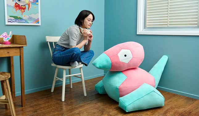 A person sits on a chair as they look down at the Porygon on the floor.