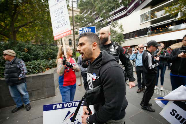 Provacateur Avi Yemini marches in front of a sign that says "protect our democracy from Islam."